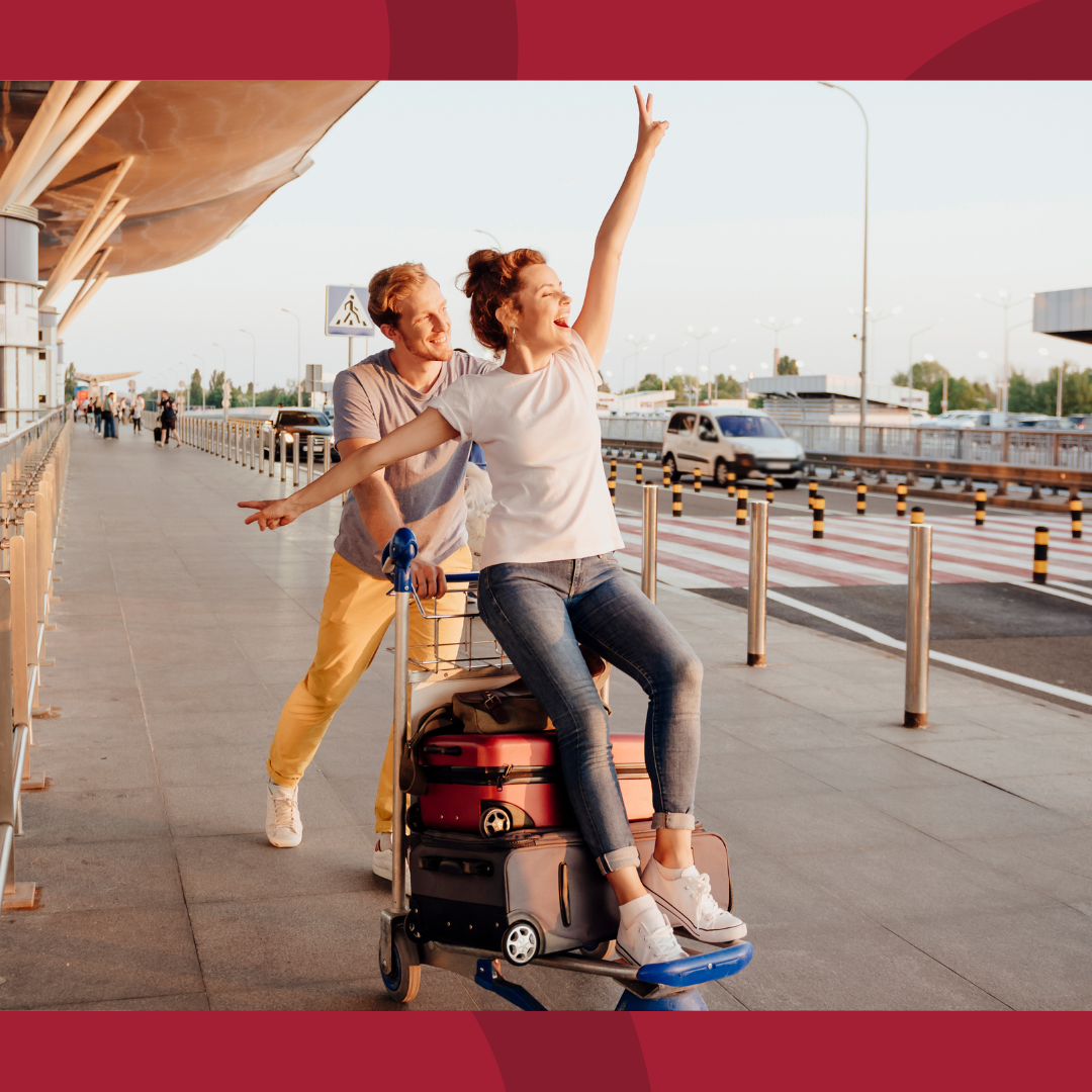 A man pushing a luggage cart with a woman sitting on the luggage.